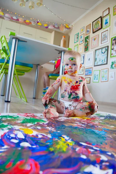 Bebé niño dibuja con pinturas de colores manos, pies sucios y dedos — Foto de Stock