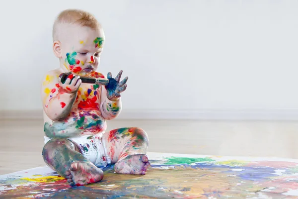 Bebé niño dibuja con pinturas de colores manos, pies sucios y dedos — Foto de Stock