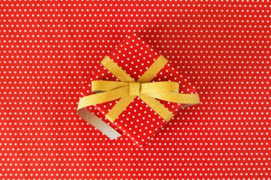 Kırmızı benekli arka planda altın kurdeleli kırmızı hediye.