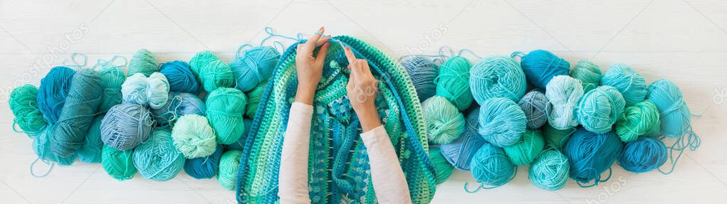 Women's hands are large. Woman crochets. Yarn of green, turquois