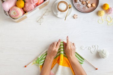 Sıcak, sade bir ortam. Kadın örgü hobisi. Sıcak renklerde iplik. Pembe, şeftali, bej, beyaz ve yeşil. Bir kadın süveteri örme sürecinin başlangıcı.