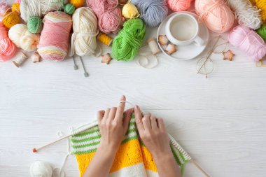 Sıcak, sade bir ortam. Kadın örgü hobisi. Sıcak renklerde iplik. Pembe, şeftali, bej, beyaz ve yeşil. Bir kadın süveteri örme sürecinin başlangıcı. İplik çerçevesi.