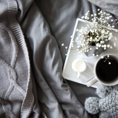 Yatakta sabah kahvaltısı. Gri yatak. Altın tepsi, İskandinav tarzı. Siyah kahve ve sütlü sütçü. Gri vazoda çiçekler.