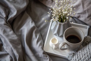 Yatakta sabah kahvaltısı. Gri yatak. Altın tepsi, İskandinav tarzı. Siyah kahve ve sütlü sütçü. Gri vazoda çiçekler.