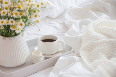 Yatakta sabah kahvaltısı. Beyaz yatak. Altın tepsi, İskandinav tarzı. Siyah kahve ve sütlü sütçü. Vazodaki papatyalar. Beyaz küçük çalar saat