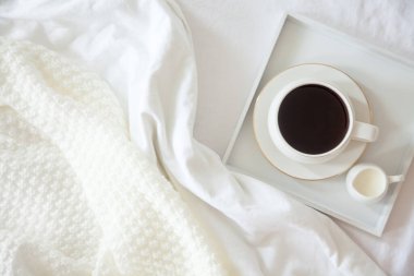 Yatakta sabah kahvaltısı. Beyaz yatak. Altın tepsi, İskandinav tarzı. Siyah kahve ve sütlü sütçü. Vazodaki papatyalar. Beyaz küçük çalar saat