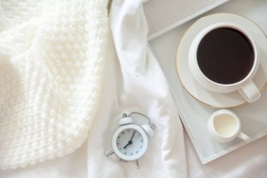 Yatakta sabah kahvaltısı. Beyaz yatak. Altın tepsi, İskandinav tarzı. Siyah kahve ve sütlü sütçü. Vazodaki papatyalar. Beyaz küçük çalar saat