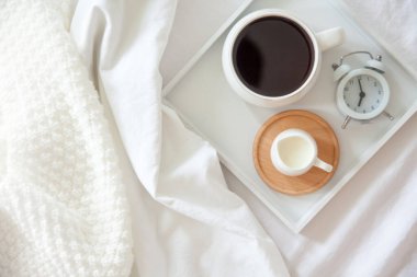 Yatakta sabah kahvaltısı. Beyaz yatak. Altın tepsi, İskandinav tarzı. Siyah kahve ve sütlü sütçü. Vazodaki papatyalar. Beyaz küçük çalar saat