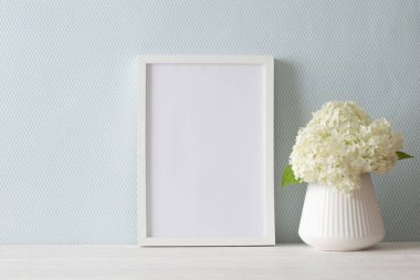 İskandinav tarzında beyaz bir vazo mavi duvarın yanında duruyor. Bir buket yeşil ortanca. Tahta masa.