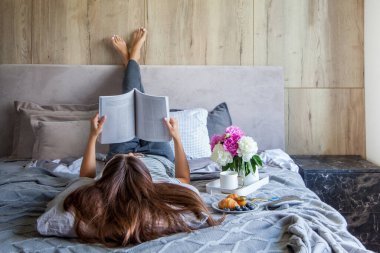 Kitap ya da gazete okuyan ve sabahları yatakta kahve içen bir kadın. Kız baş aşağı yatıyor..