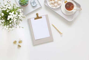 Kadın işyerindeki beyaz ve altın kırtasiyesi. Mücevher, bilezik ve yüzükler. Vazoda çiçekler, çay ve bizet. Çalar saat ve domuz kumbarası. İskandinav İskandinav tarzı.