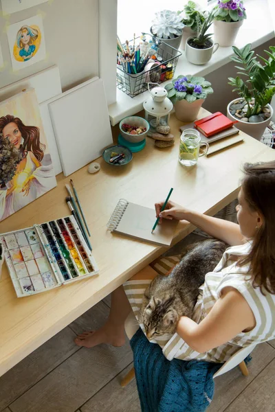 소녀는 직장에 앉아서 초상화를 물감으로 그리고 작품들은 고양이를 페인트 꽃들이 — 스톡 사진