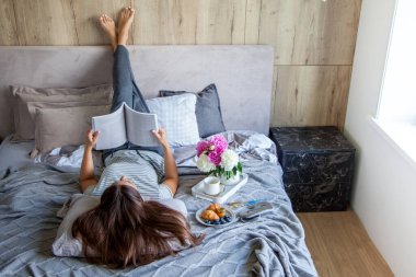 Kitap ya da gazete okuyan ve sabahları yatakta kahve içen bir kadın. Kız baş aşağı yatıyor..