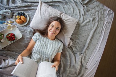 Kitap ya da gazete okuyan ve sabahları yatakta kahve içen bir kadın.
