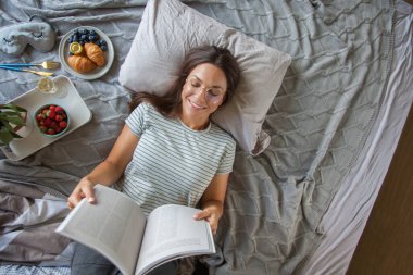 Kitap ya da gazete okuyan ve sabahları yatakta kahve içen bir kadın.