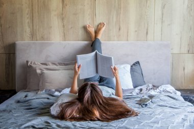 Kitap ya da gazete okuyan ve sabahları yatakta kahve içen bir kadın. Kız baş aşağı yatıyor..