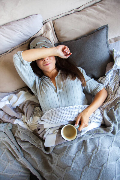 Young beautiful girl on the bed drinking coffee. Gray bedding. Eye patch.