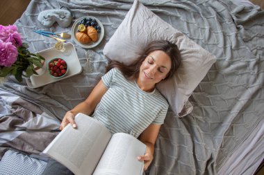 Kitap ya da gazete okuyan ve sabahları yatakta kahve içen bir kadın.