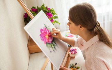 Kafkasyalı genç güzel kız ressamın en iyi görüntüsü masasında oturan pembe çiçek ve şakayık desenli boya malzemeleri ve kuru pastel boyalarla çizim yapıyor. Yaratıcılık ve hobi kavramı
