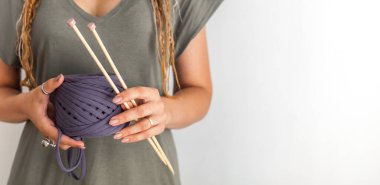 Bir kadının elinde büyük bir örgü iğnesi ve örgü ipliği bulunur. Beyaz arkaplan.