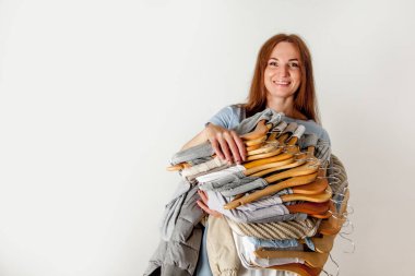 Elinde sıralanmış pamuk ve yün gömlekli ahşap askılar tutan mutlu beyaz kadın. Kuru temizleme. Alışverişe. Çamaşır servisi. Uzayı kopyala Tekstil. Temiz kıyafetler..