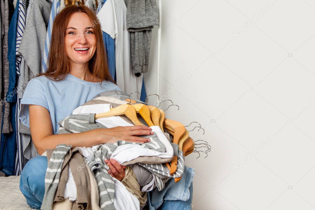 Happy caucasian woman holding bunch of wooden hangers with sorted cotton and wool shirts. Dry cleaning. Shopping. Laundry service. Copy space. Textile. Clean clothes.