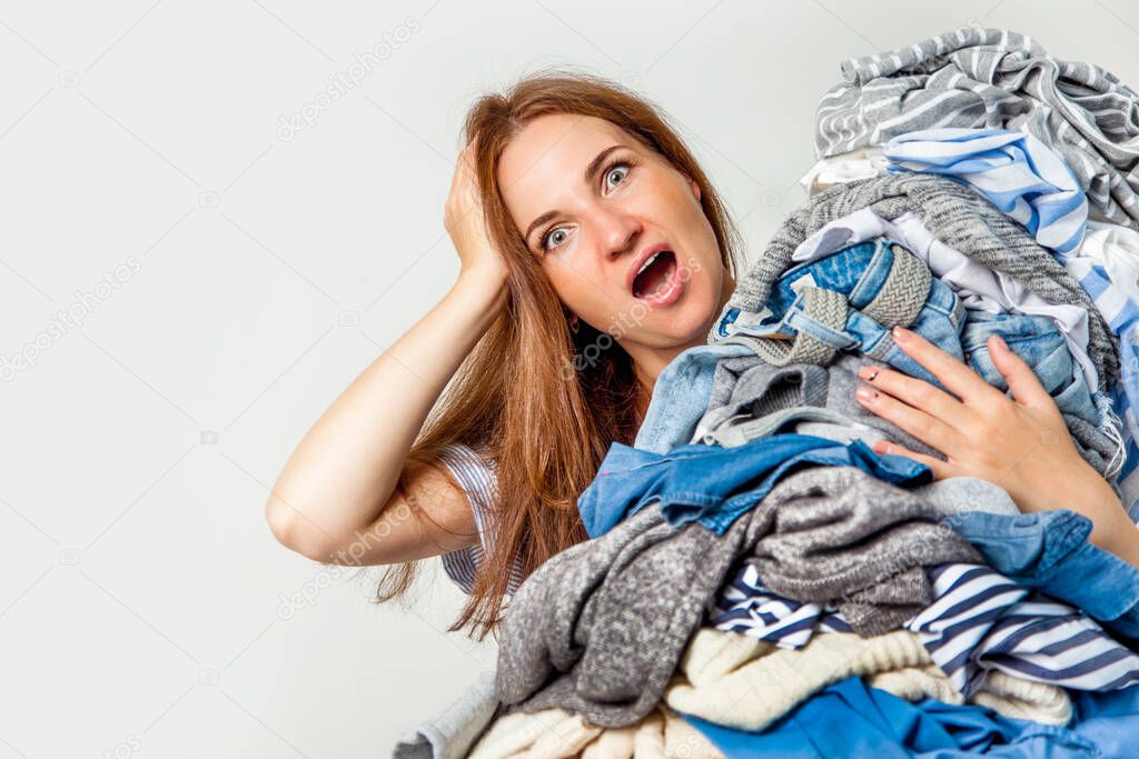 Shocked caucasian housewife holding heap of dirty clothing. Laundry. Chaos concept. Background. Busy woman.