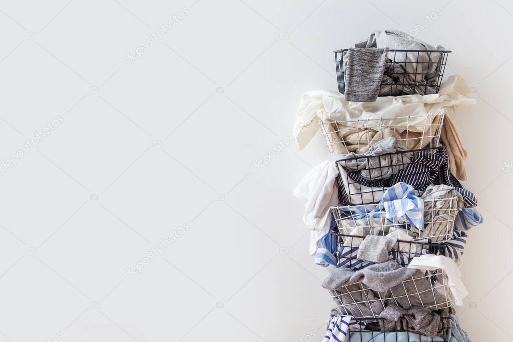 One row of stacked metal laundry basket with full of clothing on white background. Nobody. Copy space. Textile. Mixed dirty wardrobe. Decluttering concept. White background.