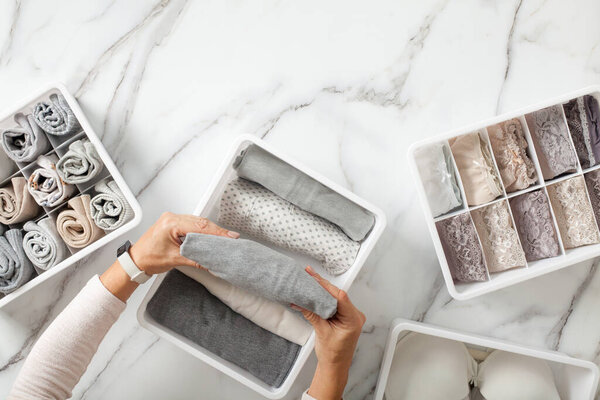 Woman hands neatly folding underwears and sorting in drawer organizers on white marble background. Closet tidying and decluttering concept. Copyspace. Hypoallergenic fabric. Organic cotton.