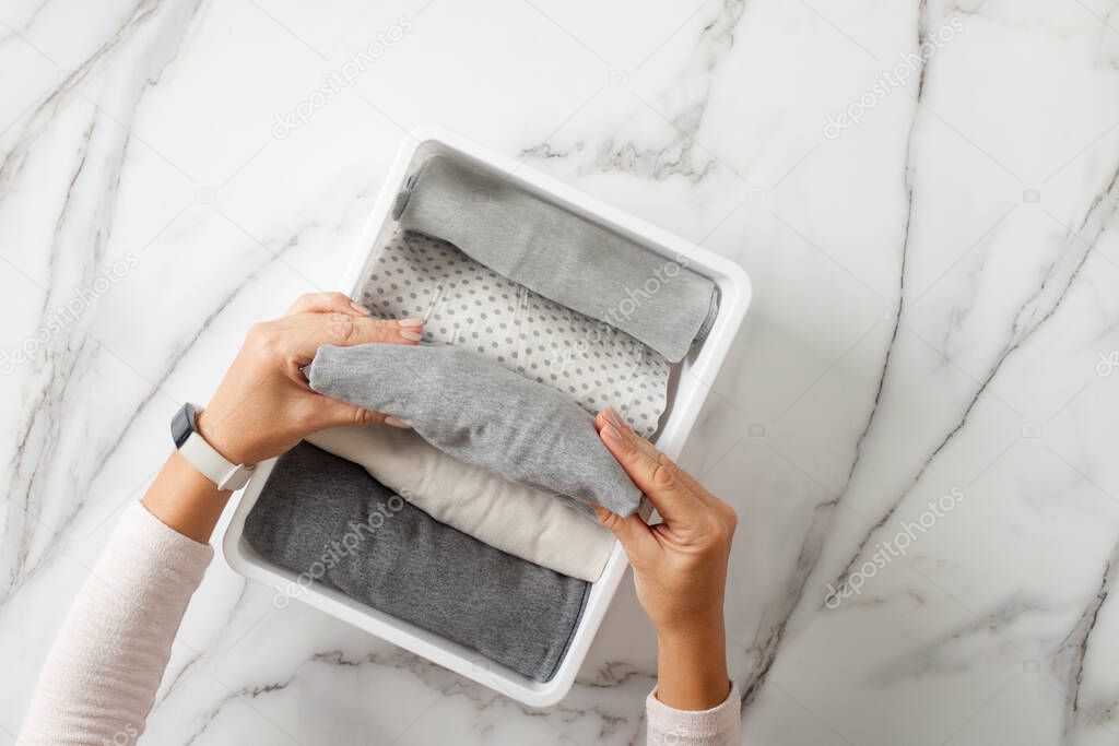 Woman hands neatly folding underwears and sorting in drawer organizers on white marble background. Closet tidying and decluttering concept. Copyspace. Hypoallergenic fabric. Organic cotton.