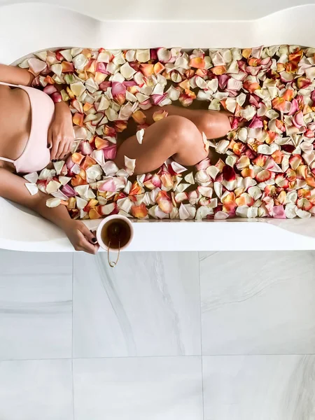 소녀는 분홍색 꽃잎이 욕조에 위에서 머그에서 마셔라 욕조에서 — 스톡 사진