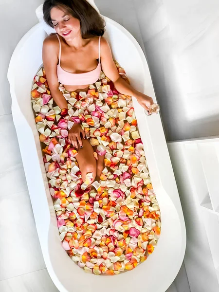 소녀는 분홍색 꽃잎이 욕조에 위에서 머그에서 마셔라 욕조에서 — 스톡 사진
