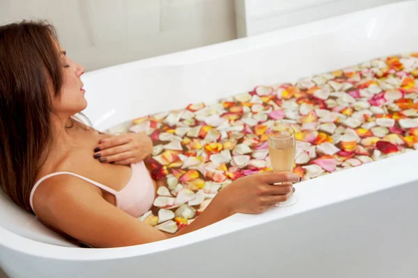 年轻漂亮的姑娘躺在有粉色花瓣的浴缸里 从上面看喝粉红色杯子里的茶 在一个大的圆形的白色浴缸里 — 图库照片