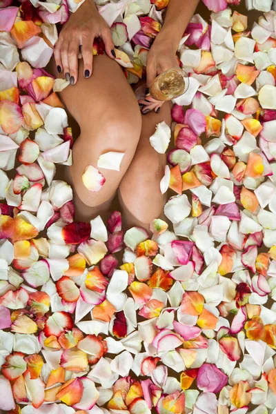 Genç ve güzel bir kız pembe yapraklarla bir banyoda yatıyor. Yukarıdan bak. Pembe bardaktan çay içiyor. Büyük yuvarlak beyaz bir küvette.