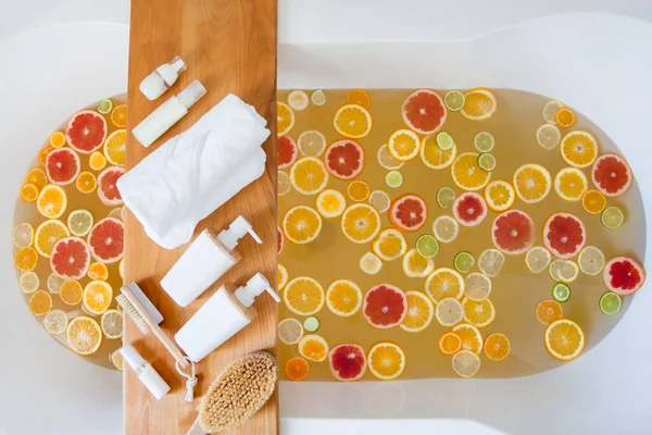 水で満たされた浴槽 木のトレイに新鮮な柑橘類や美容製品の混合スライス 有機成分と天然温泉成分 デトックス柑橘系のバストリートメント 自然と健康の概念 — ストック写真