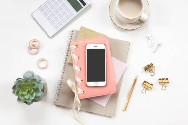 Kırtasiye seti, kahve, kulaklık ve saksıda bitki örtüsü olan minimum ofis masası. Not defteri, kalem, yapışkan rulo, iPod, bitki ve beyaz zemin üzerinde düz beyaz kahve olan kadın çalışma alanı.