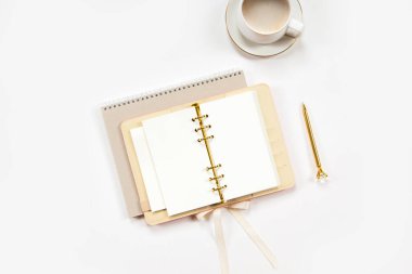 Üst kattaki defter, temiz çarşaflı, altın kalemli, bej derili günlük, beyaz masadaki bir fincan düz beyaz kahve. Kopya alanı olan eğitim ya da iş geçmişi. Minimalist ofis çalışma alanı
