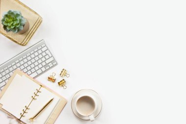 Ofis masasının klavyeli aksesuarları altın tepside kahve ve beyaz arka planda bitki. Evrak işleri için temiz çarşaflı günlük, altın kalem ve kağıt makası. Boşluğu kopyala