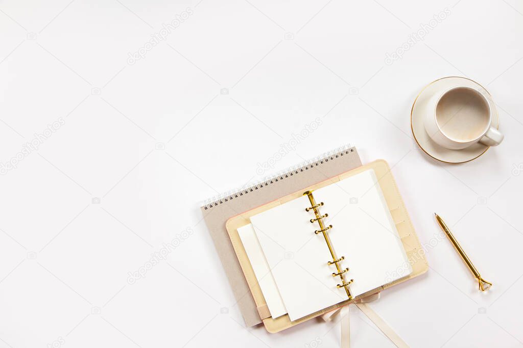 Top view notepad and beige leather covered personal diary with clean sheets, gold pen, cup of flat white coffee on white desk. Education or job background with copy space. Minimalist office workspace