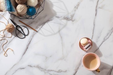 Farklı renkte yün yumakları ve beyaz mermer zeminde makas yakınında şık ağ sepetine ahşap örgü kancası takılı kış eşarbı. El işi yün elbiseler. Geleneksel hobi. Boşluğu kopyala