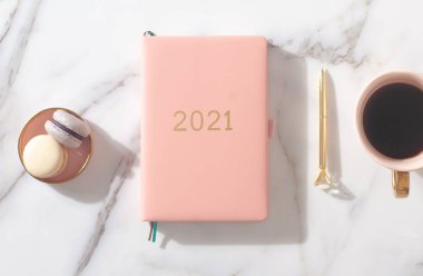 Pink coral colored diary for the year 2021, pen, coffee latte, macaron cookie and straw woven placemat on white marble background. New year planning concept. Minimalistic workstation. Copy space. clipart