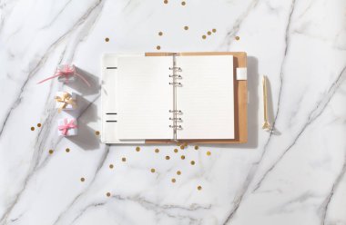 Metnin, kalemin, kahve fincanın, sütün, pembe kurdeleli küçük hediye kutun ve beyaz mermer masanda altın parıltılar için boş sayfaların olduğu defter. Yeni yıl ve Noel konsepti, en iyi manzara. Bayram kutlamaları