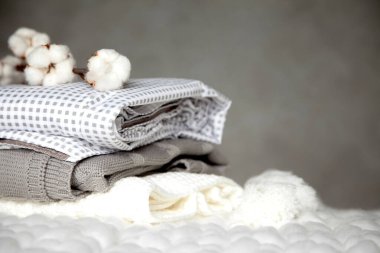 Farklı dizayn modelleri olan katlanmış sıcak battaniye yığını ve gri arka planda pamuk dalı. Örgü battaniyeler. Doğal bitki bazlı tekstil lifleri üretimi. Üretim. Organik ürün