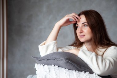 Sıcak bej bornozlu, güzel bir gülümsemesi olan genç bir kadın katlanmış çarşaf yığınına yaslanıyor. Doğal ve organik pamuktan yatak. Uzayı kopyala Üretim. Otel endüstrisi.