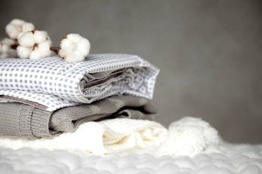 Farklı dizayn modelleri olan katlanmış sıcak battaniye yığını ve gri arka planda pamuk dalı. Örgü battaniyeler. Doğal bitki bazlı tekstil lifleri üretimi. Üretim. Organik ürün