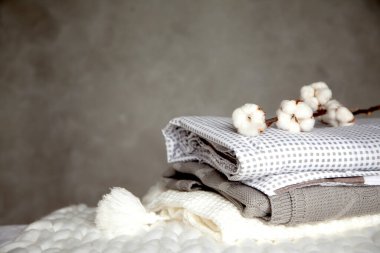 Farklı dizayn modelleri olan katlanmış sıcak battaniye yığını ve gri arka planda pamuk dalı. Örgü battaniyeler. Doğal bitki bazlı tekstil lifleri üretimi. Üretim. Organik ürün