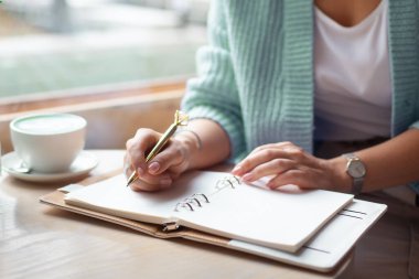 İyi giyimli kadın elinde altın kalemle not defterine altın kalemle notlar yazarken pencerenin yanında mavi latte içiyor. Evde çalışan serbest çalışan bir gazeteci. Gelecek planlama konsepti. Boşluğu kopyala