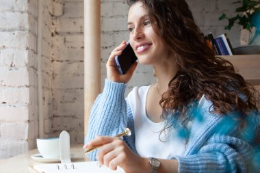 Sıcak mavi örgü süveterli dalgalı saçlı genç bir kadın telefonla konuşuyor ve notlar yazıyor. Bu sırada da doğal bezelye çayından yapılmış sağlıklı sıcak mavi kahve lattesi içiyor. Güzellik ve refah