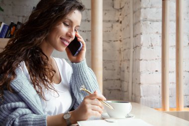 Sıcak mavi örgü süveterli dalgalı saçlı genç bir kadın telefonla konuşuyor ve notlar yazıyor. Bu sırada da doğal bezelye çayından yapılmış sağlıklı sıcak mavi kahve lattesi içiyor. Güzellik ve refah