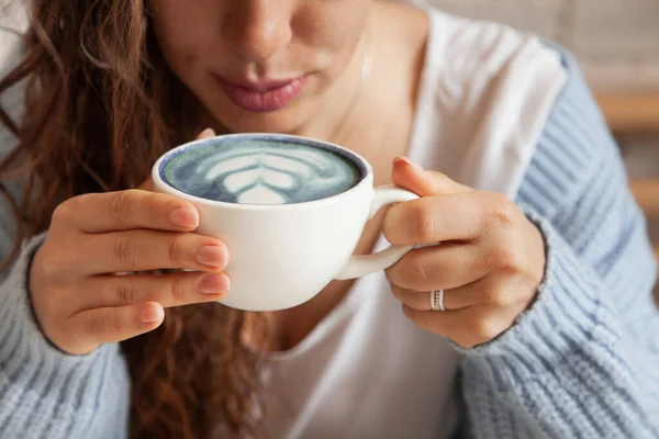 快乐的年轻女人 穿着针织的暖和毛衣 手牵着一杯健康的热蓝色咖啡拿铁 蓝色咖啡拿铁 用新鲜咖啡豆和蓝海蝴蝶茶制成 福利概念 — 图库照片